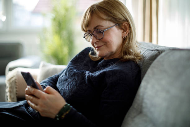 istock Smiling senior woman using mobile phone at home 1299493478