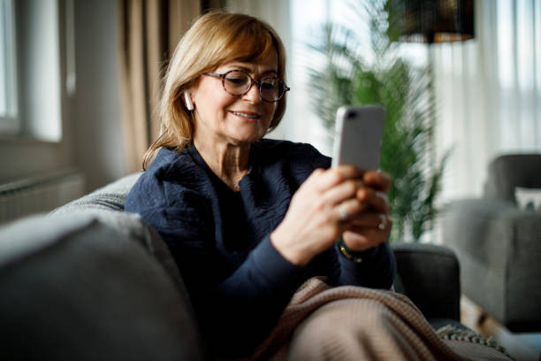 istock Smiling senior woman with bluetooth headphones using mobile phone at home 1299493489