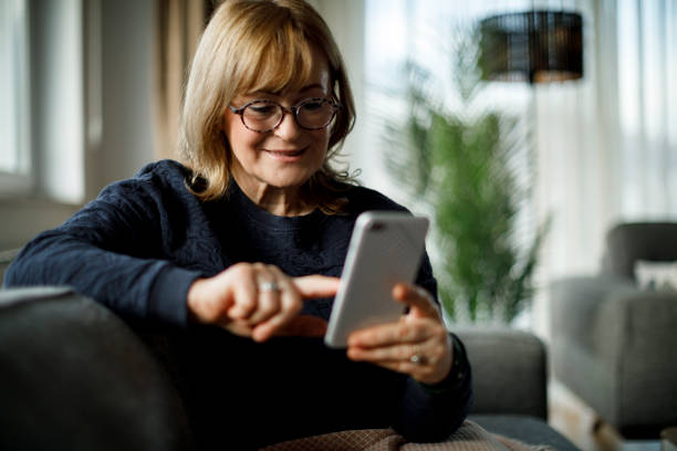 istock Smiling senior woman using mobile phone at home 1299493503