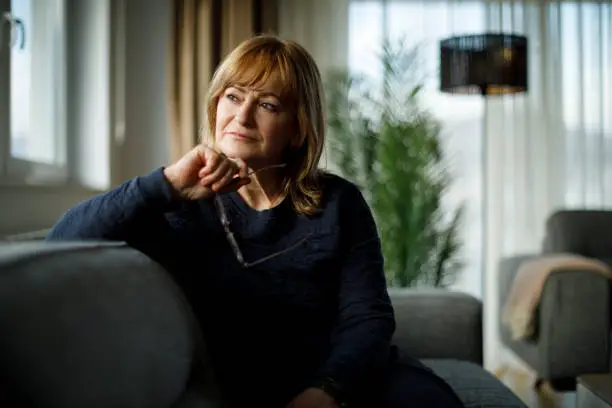 Photo of Portrait of worried senior woman sitting on sofa at home