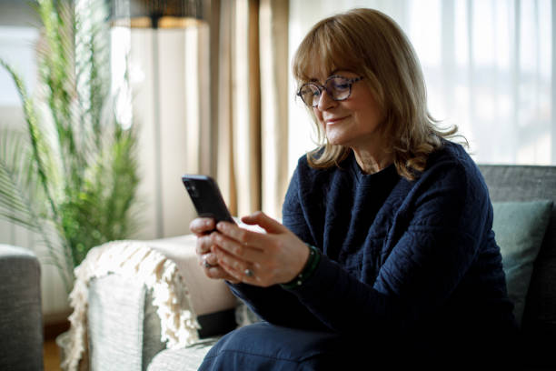 istock Smiling senior woman using mobile phone at home 1299493554
