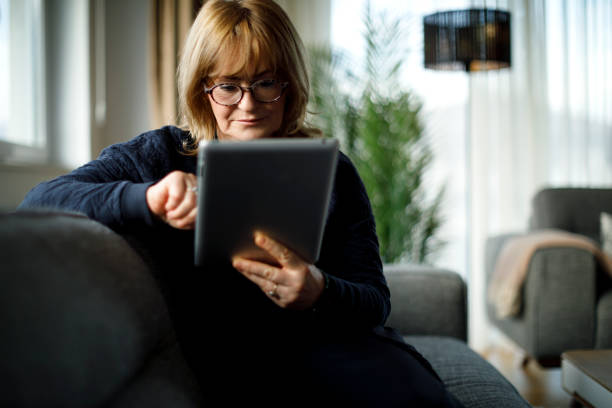 istock Senior woman sitting on sofa and using digital tablet at home 1299493699