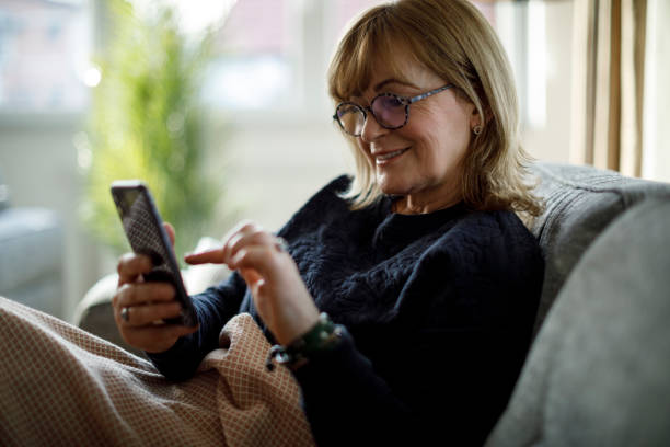 istock Smiling senior woman using mobile phone at home 1299493737