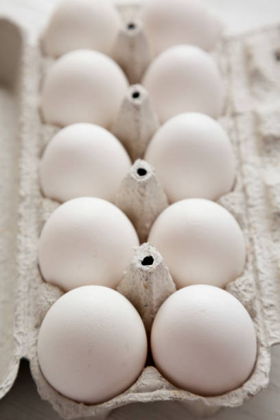 istock Uncooked Organic White Eggs in a paper box on a white wooden background, side view. Close-up. 1299493742