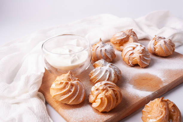 istock Choux pastry profiteroles, sprinkled with powdered sugar, on a wooden board on a white background. 1299493782
