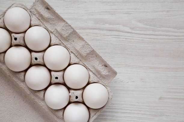 istock Uncooked Organic White Eggs in a paper box on a white wooden surface, top view. Flat lay, overhead, from above. Copy space. 1299493804