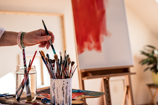 Artist choosing paintbrush during working on her abstract paintings at art studio.