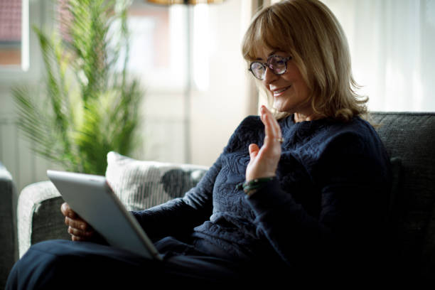 istock Smiling senior woman using digital tablet for video call at home 1299493906