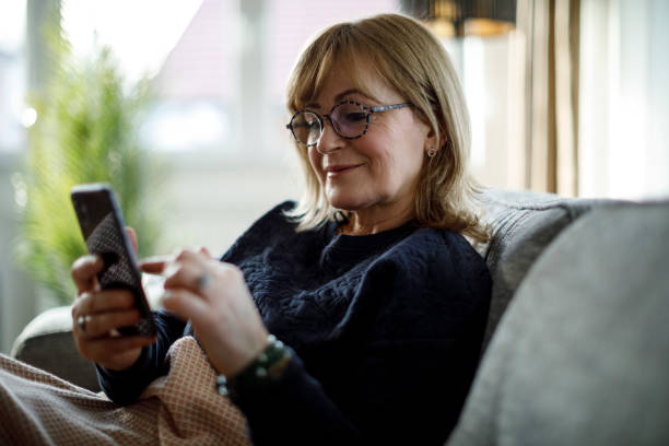 istock Smiling senior woman using mobile phone at home 1299493938