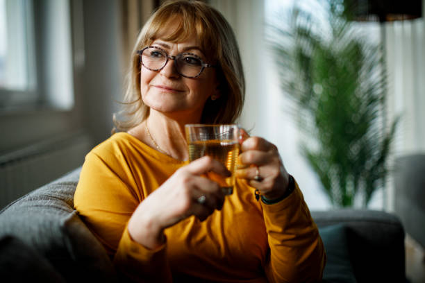 retrato de hermosa mujer mayor sonriente sonriente sentada en el sofá y bebiendo té en casa - infusión té bebida fotografías e imágenes de stock