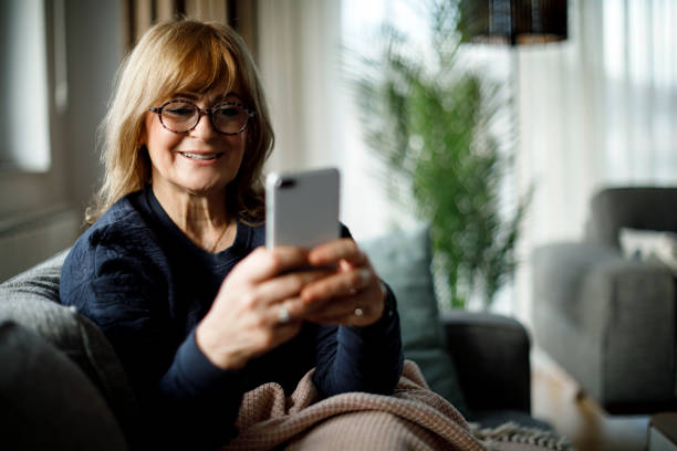 istock Smiling senior woman using mobile phone at home 1299494534