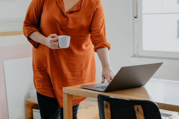 istock Anonymous Plus Size Woman Drinking Coffee and Using her Laptop for Work at Home 1299495986