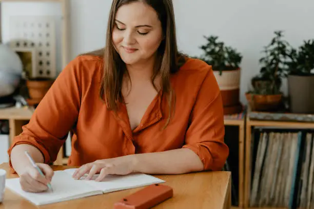 Photo of Beautiful  plus size Woman Sitting in her Living Room and Writing a Diary