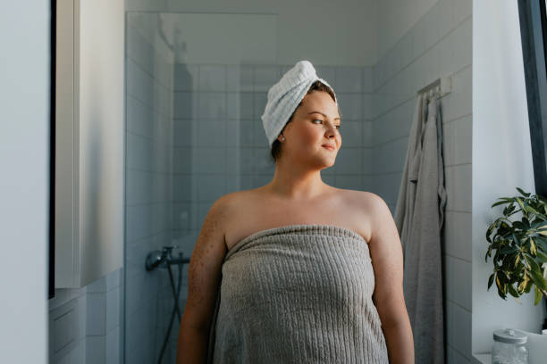 verticale d’une femme en surpoids heureuse restant dans la salle de bains après une douche relaxante - women bathtub bathroom water photos et images de collection