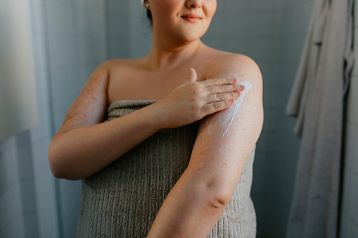 Mujer con sobrepeso anónima aplicando loción corporal después de la ducha photo