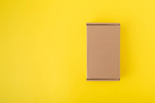 istock Cardboard box on yellow background top view. Craft packaging. Copy space. Mock up 1299496573