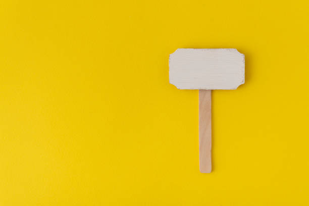 istock Wooden pointer on yellow background. Information plate. Wooden plate. Copy space. Mock up 1299496777