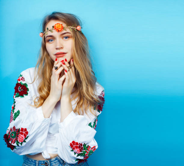 young pretty blond girl posing on blue background, fashion style hippie boho flowers on head stock photo