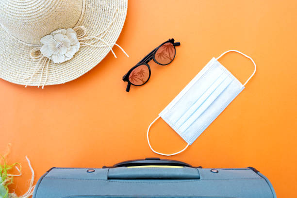 istock Flat lay with copy space, a luggage, face mask, sun hat, sunglasses and a scarf are arranged on an orange background. Travel concept during the Covid-19 pandemic. 1299498761