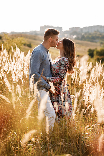 beautiful young couple kissing in a field with grass at sunset. stylish man and woman having fun outdoors. family concept. copy space