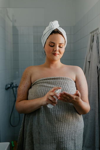 A cheerful  plus size woman applying body lotion after a shower in the morning.