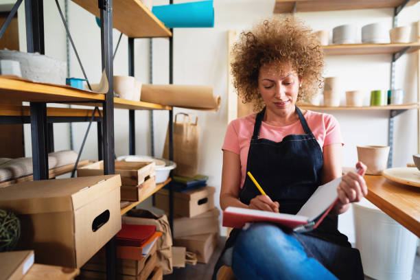 istock Smiling craftswoman with a planner book in her creative pottery studio 1299501469