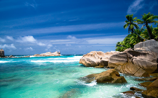 Blue sea and exclusive remote beach in Seychelles islands (La Digue) wih turquoise water and few people swimming and playing