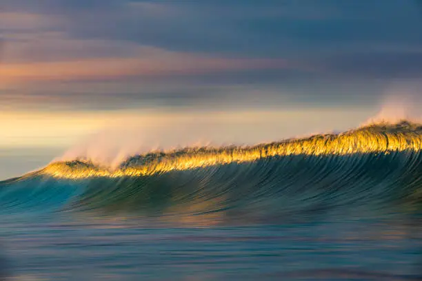 Photo of Cresting wave breaking in brilliant orange and golden morning light