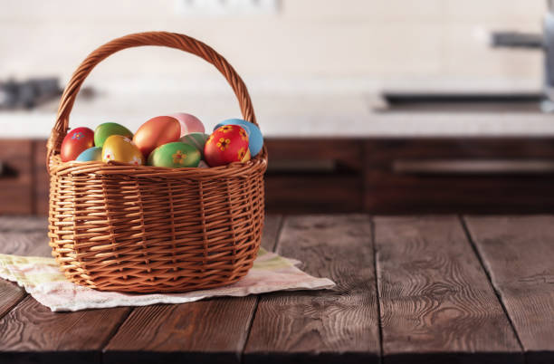 cesto di vimini con uova colorate di pasqua sul tavolo in legno della cucina. composizione pasquale primaverile. copiare lo spazio per testo o progettazione. - wood eggs easter easter egg foto e immagini stock