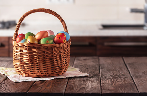 Wicker basket with Easter colorful eggs on kitchen wooden table. Spring Easter composition. Copy space for text or design.
