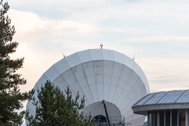 istock Big satellite dish antennas hidden in green pine tree forest communication center on bright blue white background 1299516103