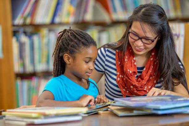 Thanks for helping me, teacher! A female teacher of Asian ethnicity is helping her student with a book. They are at their school library. literacy photos stock pictures, royalty-free photos & images