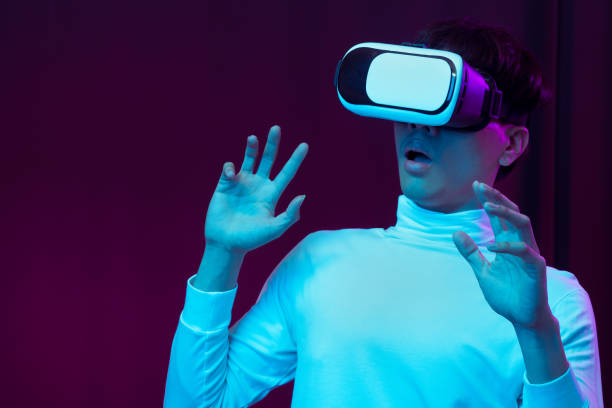 istock Excited asian young man wearing VR headset in neon light, Future technology concept 1299518969