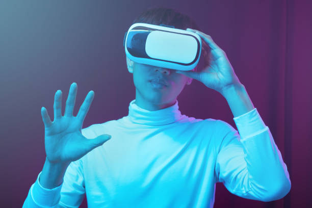 istock Young asian man wearing virtual reality goggles watching 360 degree video in neon light, Technology concept 1299518971