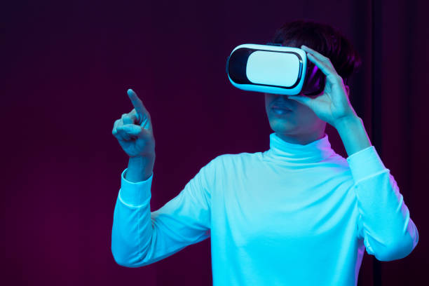 istock Young asian man wearing virtual reality goggles watching 360 degree video in neon light, Technology concept 1299518982