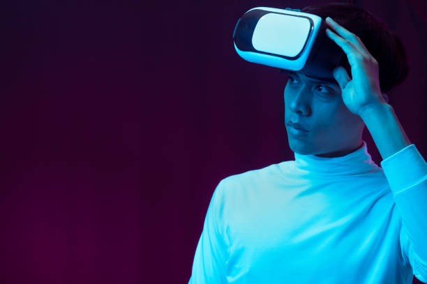 istock Young asian man wearing virtual reality goggles watching 360 degree video in neon light, Technology concept 1299518994