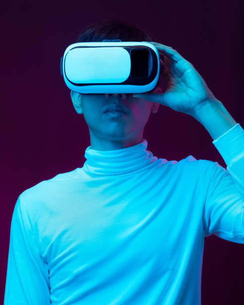 istock Young asian man wearing virtual reality goggles watching 360 degree video in neon light, Technology concept 1299518999