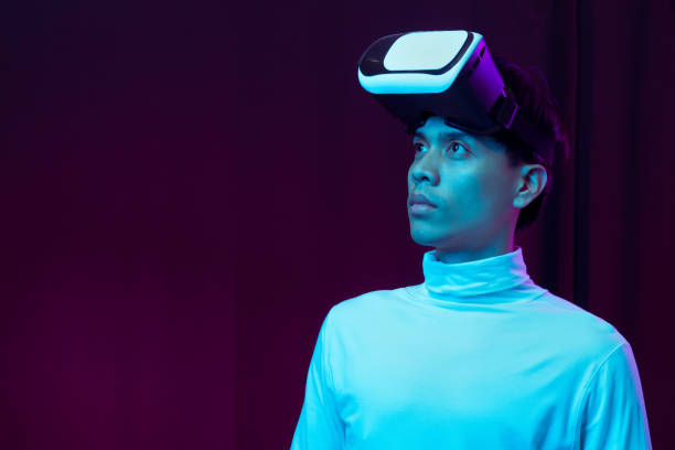 istock Young asian man wearing virtual reality goggles watching 360 degree video in neon light, Technology concept 1299519000