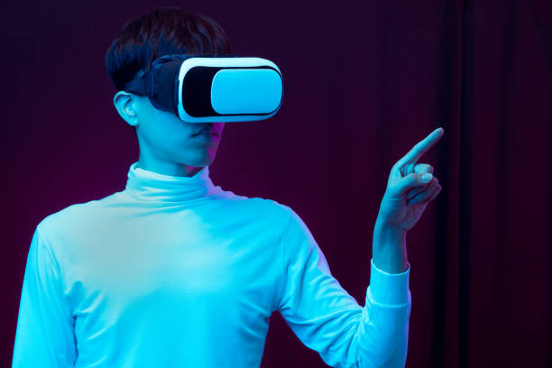 istock Young asian man wearing virtual reality goggles watching 360 degree video in neon light, Technology concept 1299519567
