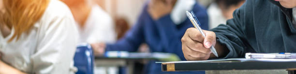 Exam at school with student's taking educational admission test in class, thinking hard, writing answer in university classroom, education and world literacy day concept