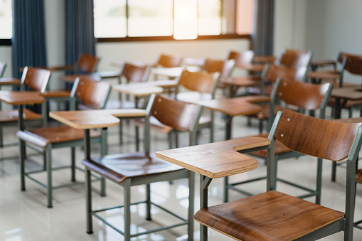 Empty university classroom with many wooden chairs. Wooden chairs well arranged in the college classroom. Empty classroom with vintage tone wooden chairs. Back to school concept.