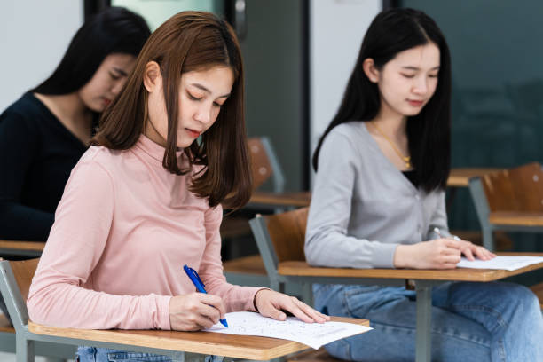 istock Young female university students concentrate on doing examinations in the classroom. Girl students seriously write the exercise of the examinations in the classroom. 1299531195