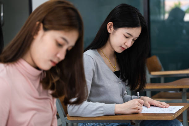 istock Young female university students concentrate on doing examinations in the classroom. Girl students seriously write the exercise of the examinations in the classroom. 1299531295
