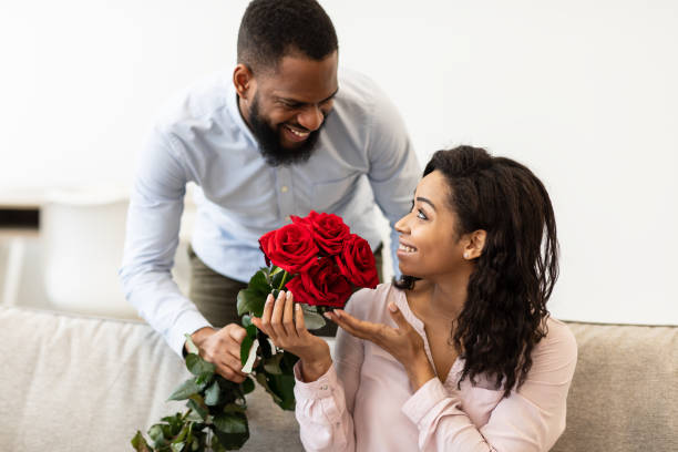 jeune homme noir donnant des roses rouges à la femme - anniversary couple rose black photos et images de collection