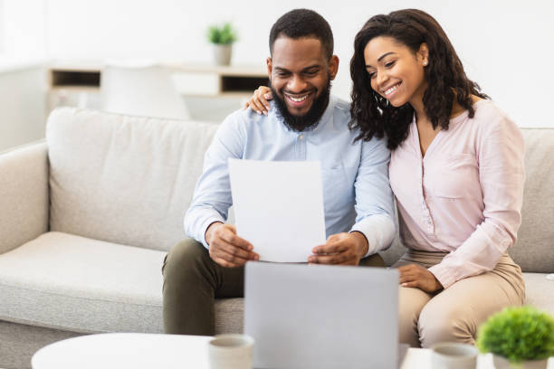 istock Positive black couple reading letter at home, sitting on couch 1299554554