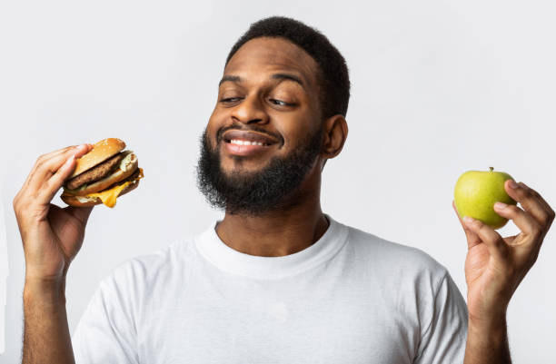 istock Black Guy Holding Burger And Apple Choosing Food, White Background 1299554766