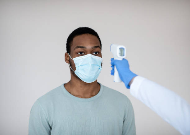 istock Checking temperature before covid-19 vaccination. Doctor aiming electronic thermometer at black man in health centre 1299555090
