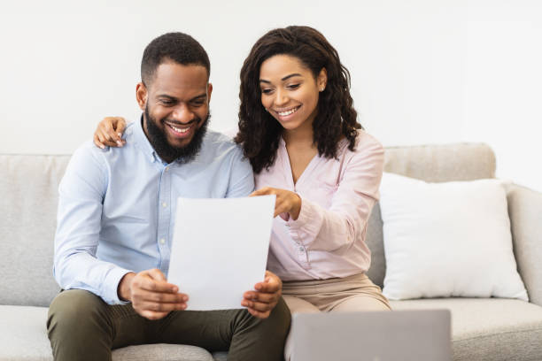 istock Smiling afro couple reading documentation at home, checking agreement 1299555675