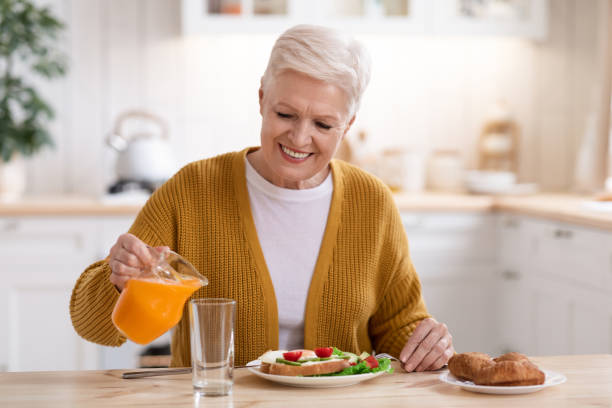 istock Attractive old lady pouring juice, having lunch in kitchen 1299555689