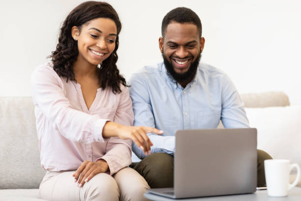 istock African american couple sitting on couch, using laptop 1299556000